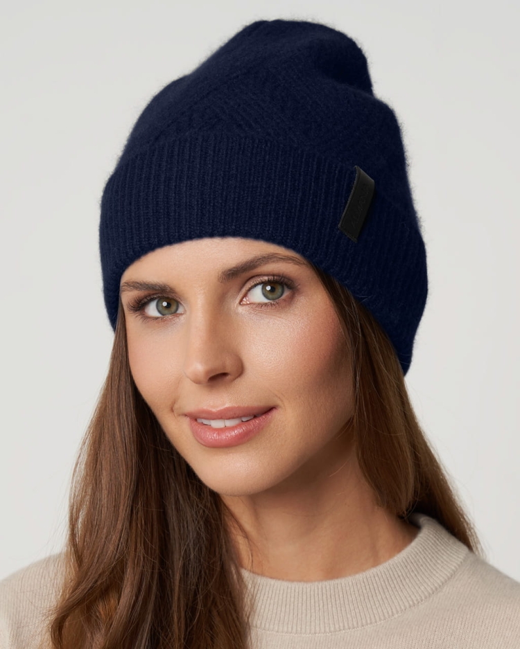 Granatowa kaszmirowa czapka zimowa typu beanie z wywiniętym brzegiem, prezentowana na modelce.
